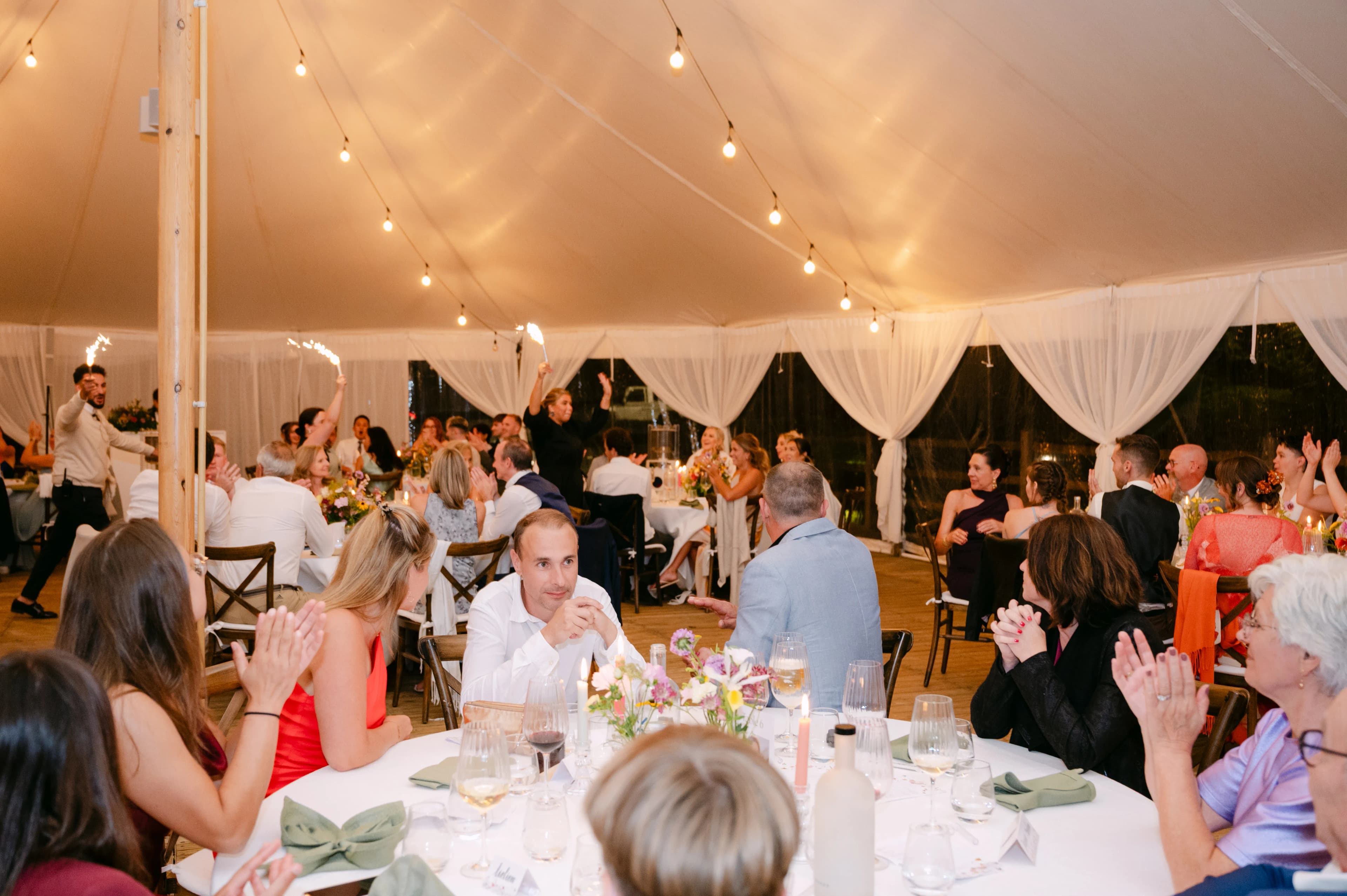 Gasten aan tafels in tent met lichtjes - vegan trouwfeest